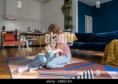 Fürsorgliche Mutter, die auf dem Boden sitzt und den kleinen Jungen umarmt, der zärtliche Liebe, Vertrauen, Unterstützung, Genieß den Moment Stockfoto