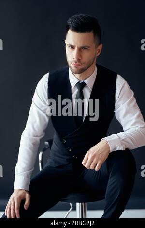 Portrait von Stattlichen zuversichtlich Mann sitzt auf einem Stuhl und auf schwarzem Hintergrund posiert Stockfoto