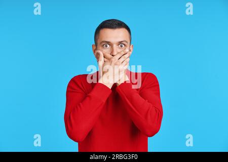 Mann, Mund mit den Händen über blauen Hintergrund schockiert. Emotionen und geheime Konzept Stockfoto