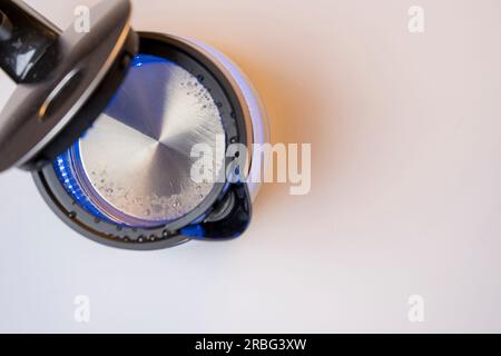 Ein neuer elektrischer Wasserkocher aus rotem, modernem Glas mit offenem Deckel, sprudelndem Wasser und blauem Neonlicht. Schiebeleiste Stockfoto