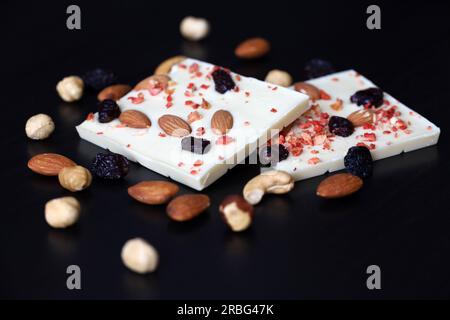 Weiße Schokolade mit getrockneten Rosinen, Zitrusfrüchten und Nüssen. Leckeres Dessert auf einem dunklen Holztisch Stockfoto