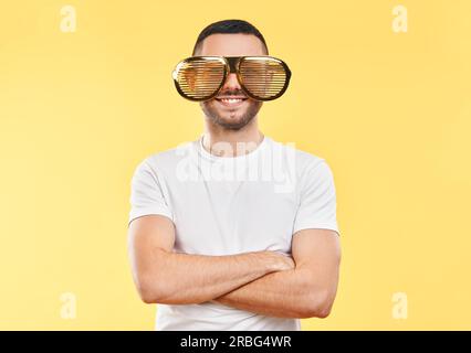Junger Mann mit lustiger Partybrille auf gelbem Hintergrund. Lustiges Konzept Stockfoto