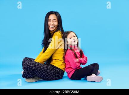 Glücklich lächelnde Mutter und ihre kleine süße Tochter posiert auf blauem Studio Hintergrund Stockfoto