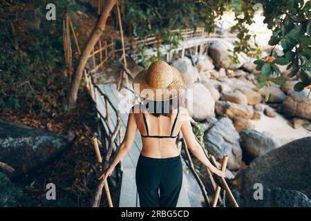 Rückblick einer jungen Frau mit Strohhut auf einer Holzbrücke auf einer tropischen Insel. Urlaub, Reisekonzept Stockfoto