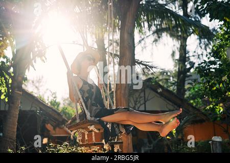 Happy barfuß Mädchen auf Schaukel im Sonnenlicht auf tropische Insel. Sorglose Frau Stockfoto