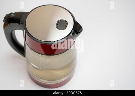 Elektrischer Wasserkocher aus Glas mit wunderschönen roten Wänden gefüllt mit Wasser für die Teezubereitung auf weißem Hintergrund mit Blick von oben. Stockfoto