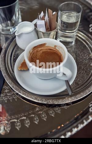Starken Espresso Kaffee mit Milch in einen Krug und ein Glas Wasser auf einem Tablett in einem Restaurant auf der Seite betrachtet nahe hohen Winkel Stockfoto