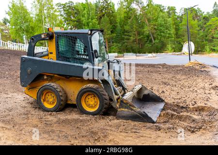 Mini-Lader mit Schaufel. Ein Lader mit Schaufel räumt die Baustelle für Bauarbeiten frei. Bodenverbesserungsarbeiten auf dem Territorium. Maschine zum Bewegen des Bodens, sa Stockfoto