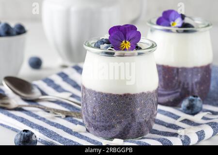 Gesundes veganes Frühstück mit Heidelbeerjoghurtparfaits mit frischen Beeren, Kokosnuss-Joghurt, Chia-Pudding und essbaren Blumen Stockfoto