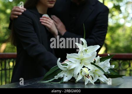 Leute in der Nähe weißer Lilien auf Grabstein auf dem Friedhof, Nahaufnahme. Beerdigungszeremonie Stockfoto