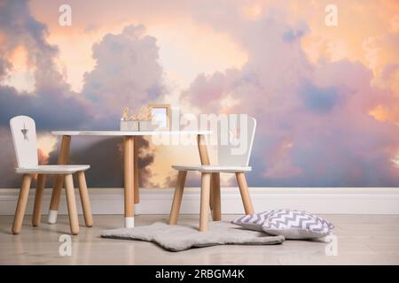 Malerischer Himmel mit Wolken als Tapetenmuster. Innenausstattung des Babyzimmers mit Tisch und Stühlen an der Wand Stockfoto