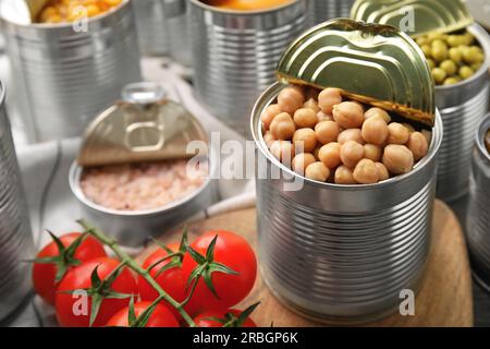 Öffnen Sie Blechdosen mit Kichererbsen und verschiedenen Produkten auf einem Holztisch, Nahaufnahme Stockfoto