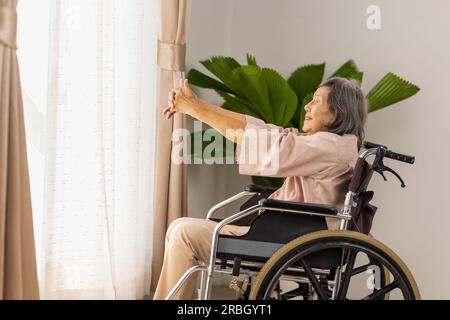 Ältere asiatische Frau, die im Wohnraum zu Hause Stretching-Übungen im Rollstuhl macht Stockfoto