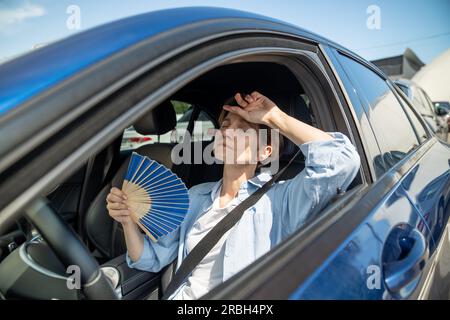 Erschöpfte Frau mittleren Alters fährt Autowellen blauer Fan leidet an Stau im Verkehr. Stockfoto
