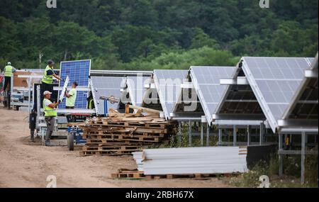 05. Juli 2023, Sachsen, Neukieritzsch: Arbeiter montieren Solarpaneele auf dem Gelände des Energieparks Witznitz. Ein gigantisches Solarkraftwerk wächst auf 500 Hektar Land auf der Deponie des ehemaligen Braunkohlebergwerks Witznitz II im Süden von Leipzig auf. Etwa 15 Prozent der ca. 1,1 Millionen aus China bezogenen Photovoltaikmodule wurden bereits installiert, und der Solarpark soll im Herbst online gehen. Mit einer installierten Leistung von 650 Megawatt hat der Park ein Drittel der Leistung des benachbarten Braunkohlekraftwerks Lippendorf (zwei Einheiten mit 920 ME) Stockfoto