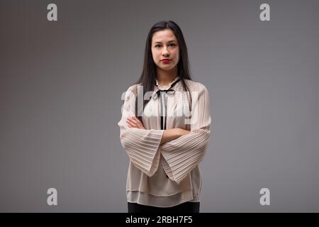 Ein halblanges Porträt einer jungen Filipina, langes Haar, verschränkte Arme, die die Situation als Boss besaß. Trägt eine beige Bluse mit schwarzem Band. Stolz, Stockfoto