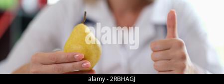 Arzt hält reife gelbe Birne in der Hand und zeigt Daumen-hoch-Zeichen Stockfoto