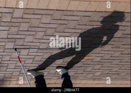 Eine gesichtslose blinde Frau läuft mit einem Stock die Straße entlang. Stockfoto