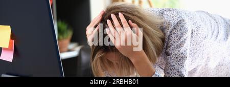 Stressige Frau beugt sich über den Tisch und hält den Kopf mit den Händen im Büro Stockfoto