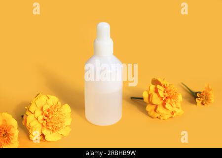 Unmarkierte weiße Plastikflasche mit Desinfektionsmittel und gelben Marigold Blüten auf gelbem goldenen Hintergrund. Natürliche organische Spa-Kosmetika und flüssiges Antimikum Stockfoto