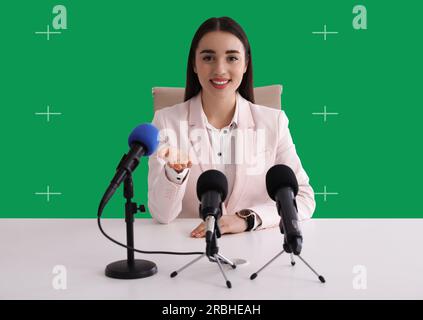 Chroma-Schlüssel-Komposition. Frau, die während der Pressekonferenz ein Interview gibt. Grüner Bildschirm hinter ihr Stockfoto