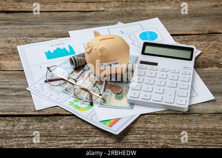 Sparschwein mit dem Wort Pension, Banknoten, Brille, Taschenrechner und Diagrammen auf Holztisch. Altersvorsorge Stockfoto
