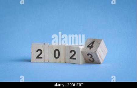 Holzwürfel oder -Blöcke auf dem Tisch, zum Jahreswechsel von 2023 bis 2024. Auf blauem Hintergrund. Stockfoto