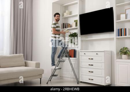 Glücklicher Mann mit Büchern auf Metall Klappleiter zu Hause Stockfoto