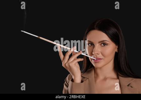 Frau mit langem Zigarettenhalter zum Rauchen auf schwarzem Hintergrund Stockfoto