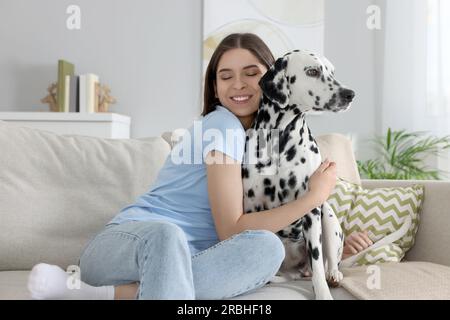 Eine schöne Frau, die ihren niedlichen dalmatinischen Hund zu Hause auf dem Sofa umarmt. Hübsches Haustier Stockfoto