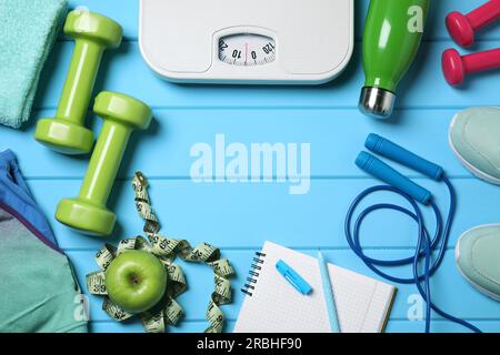 Notizbuch, Waage und Sportausrüstung auf hellblauem Holztisch, flach liegend mit Platz für Text. Persönliches Training Stockfoto