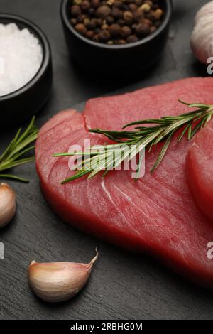 Frisches rohes Thunfischfilet mit Rosmarin und Gewürzen auf schwarzem Tisch Stockfoto