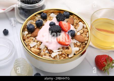 Leckeres Müsli, Joghurt und frische Beeren in der Schüssel auf dem weißen Tisch, Nahaufnahme. Gesundes Frühstück Stockfoto