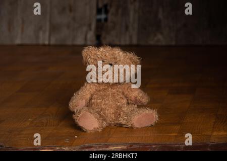 Der alte dreckige Teddybär liegt auf dem Boden in einem dunklen Raum zu Hause, verlassen und allein, Armut Stockfoto