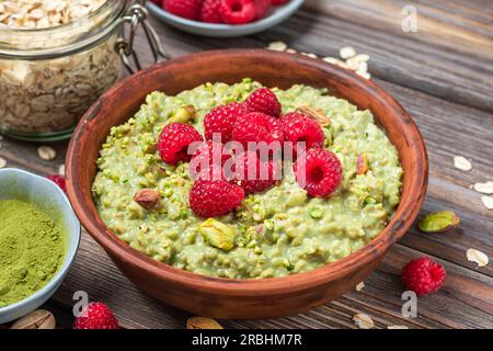 Gesundes Frühstück. Haferflocken-Matcha-Haferbrei mit frischen Himbeeren und Pistazien in einer Schüssel auf einem rustikalen Holztisch Stockfoto