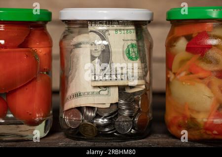 Dollar und Groschen in einem Glas geschlossen stehen neben Gemüse aus der Dose zu Hause auf einem Regal, Geld sparen, Geld in einer Dose, finanzielle Thema, tun Stockfoto
