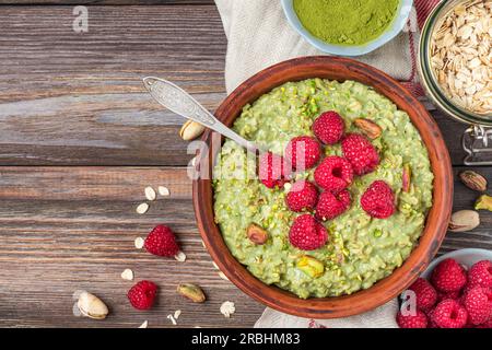 Haferflocken-Matcha-Haferbrei mit frischen Himbeeren und Nüssen in einer Schüssel für ein gesundes Diät-Frühstück auf einem rustikalen Holztisch. Draufsicht Stockfoto