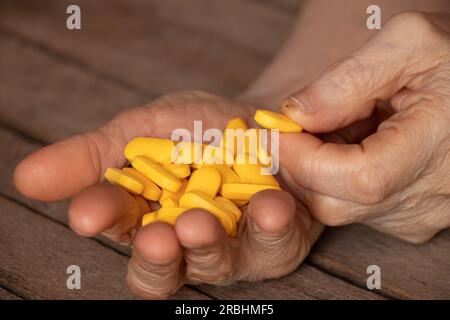 Großmutter hält gelbe Pillen in den Händen auf einem Holztisch, Pillen in den Händen und Frauen liegen und Medizin Stockfoto