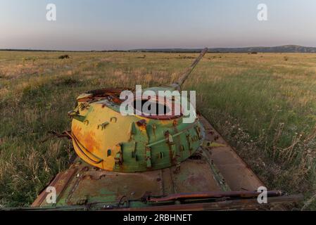 Zerstörte verrostete, verlassene und ausgebrannte Kampfpanzer in den grünen Feldern bei Sonnenuntergang. Sie können dieses Bild zur Veranschaulichung verwenden, zum Beispiel war Stockfoto