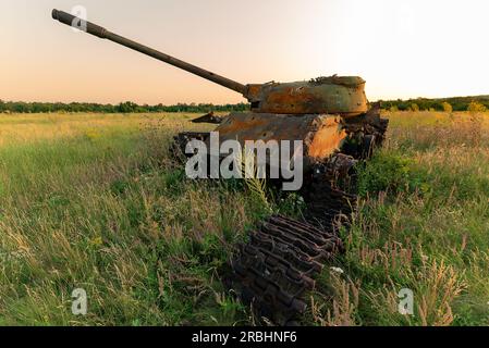 Zerstörte verrostete, verlassene und ausgebrannte Kampfpanzer in den grünen Feldern bei Sonnenuntergang. Sie können dieses Bild zur Veranschaulichung verwenden, zum Beispiel war Stockfoto