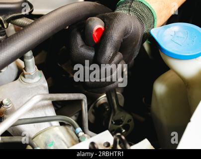 Automechaniker in schwarzen Handschuhen, die einen Automotor reparieren. Automechaniker, der an einem Motor arbeitet. Stockfoto