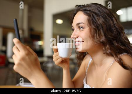 Glückliche Frau, die Kaffee trinkt, mit dem Handy, sitzt in einer Bar Stockfoto