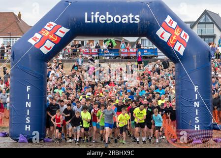 Beginn der RNLI Mulberry Harbour Charity-Tour mit rund 1800 Teilnehmern im Hafen und zurück. Junge Läufer führen Läufer vom Strand weg Stockfoto