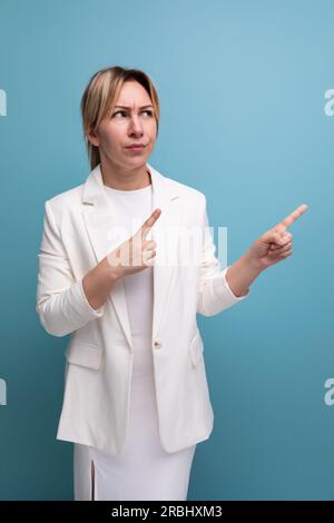 Junge, hübsche, schlanke, blonde Chefin in weißer Jacke und Kleid zeigt mit dem Finger auf das Projekt Stockfoto