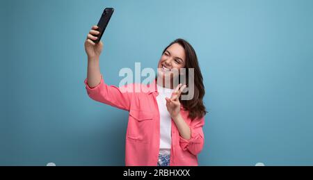 Eine moderne braune Frau mit pinkfarbenem Hemd macht Fotos mit dem Telefon im Studiohintergrund Stockfoto