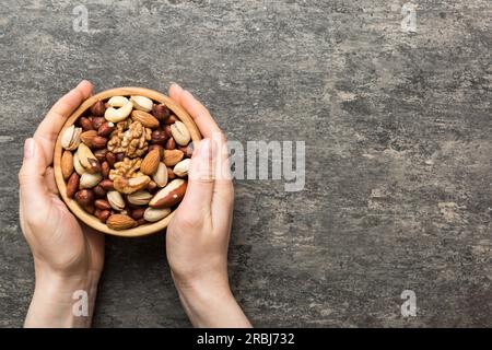 Frauenhände halten eine Holzschüssel mit gemischten Nüssen, Walnuss, Pistazien, Mandeln, Haselnüssen und Cashews. Gesundes Essen und Snack. Vegetarische Snacks dif Stockfoto