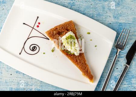 Türkisches Dessert ekmek kadayifi mit Milchcreme und Pistazien auf einem weißen Porzellanteller Stockfoto