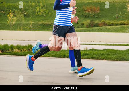 Zwei männliche Athleten, die gemeinsam ein Marathonrennen im Landschaftspark, Sommersportveranstaltung, absolvieren Stockfoto