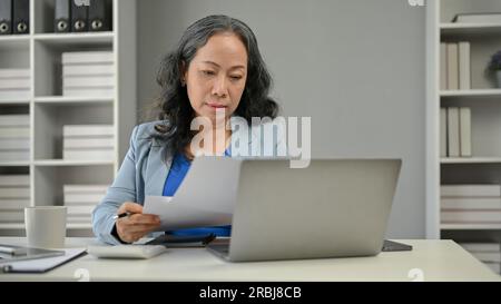 Eine aufmerksame und seriöse Geschäftsfrau oder Chefin in Asien liest Dokumente und arbeitet an ihrem Schreibtisch im Büro Stockfoto