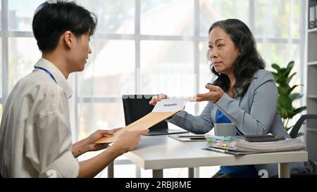 Ein junger, männlicher Büroangestellter in Asien führt ein ernstes Gespräch und gibt einem weiblichen Chefvorsitzenden im Büro ein Kündigungsschreiben. Zurücktreten, Qui Stockfoto